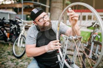 Professional bicycle mechanic in apon adjusts bike spokes and repair wheel with service tools closeup. Cycle workshop outdoor. Bicycling sport,