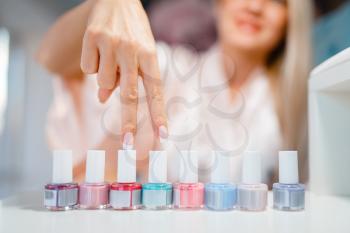 Female customer shows nail varnish choice in beauty shop. Professional manicure and pedicure service, hands and legs treatment, client in beautician salon, woman at the manicurist