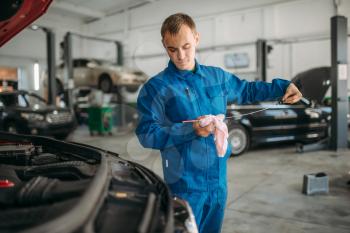 Male technician checks car engine oil level with dipstick. Auto-service, vehicle maintenance, repairman