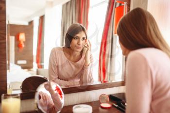 Young woman in pajama in front of the mirror in the bedroom. Female person cares for skin. Morning facial cleaning procedure