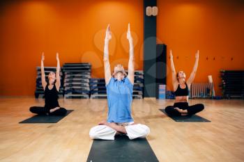 Relaxation, female group with trainer sitting in yoga pose, workout in gym. Yogi indoor