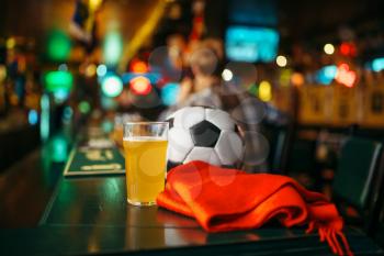 Ball, beer and red scarf on the counter in sports bar, football fans lifestyle. Tv broadcasting, watching the game concept