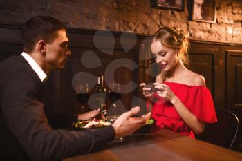 Smiling woman in red dress makes image of her man on phone camera. Beautiful love couple in restaurant, romantic evening, anniversary celebration