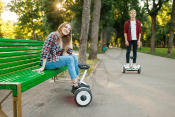 Young couple leisures with gyro board in summer park. Outdoor recreation with electric gyroboard. Transport with balance technology