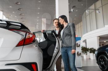 Couple choosing new car in showroom. Male and female customers looks vehicle in dealership, automobile sale, auto purchase