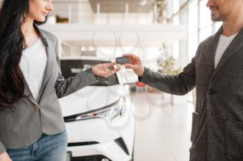 Couple buying new car in showroom, man gives the key to woman. Male and female customers choosing vehicle in dealership, automobile sale, auto purchase
