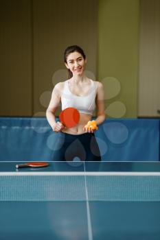 Young woman with ping pong racket and ball at the table indoors. Female person in sportswear, training in table-tennis club