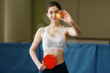 Woman with racket shows ping pong ball indoors. Female person in sportswear, training in table tennis club