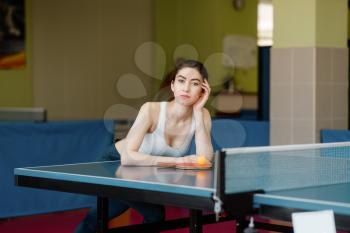 Slim woman poses at the ping pong table indoors. Female person in sportswear, training in table-tennis club