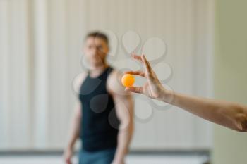 Female hand holds ping pong ball, man in sportswear on background, table-tennis training game in gym. Table tennis concept