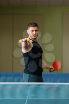 Man with racket holds ping pong balls between fingers, workout indoors. Male person in sportswear, training in table tennis club
