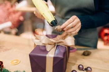 Female seller decorates gift box with fir cone, handmade wrapping and decoration process. Woman wraps present on the table, decor procedure