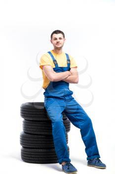 Serviceman in blue uniform sitting on tires, white background, repairman with tyres