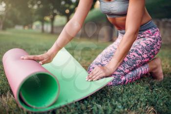 Young woman rolling yoga mat in park. Morning yogi outdoor exercise