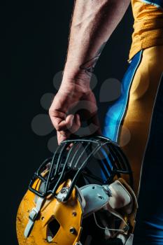 Muscular male person in uniform with american football helmet in hand. Contact sport