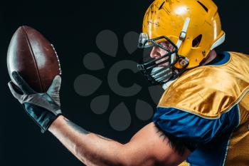 American football player with laced ball in hands, black background. Contact sport