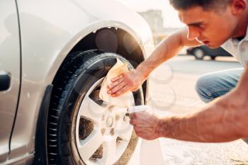 Man cleans auto with car rim cleaner, carwash. Carwashing station