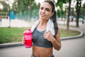 Athletic girl with sport bottle in summer park. Woman on morning workout