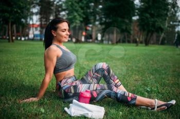 Athletic girl sitting on a grass in summer park. Woman relax on morning workout