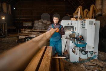 Carpenter in uniform works on woodworking machine, lumber industry, carpentry. Wood factory