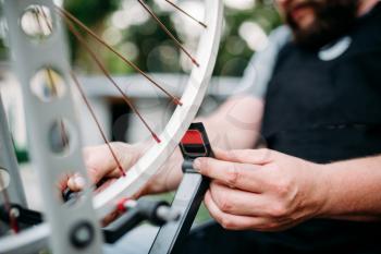Professional bicycle mechanic hands adjusts bike spokes and repair wheel with service tools closeup. Cycle workshop outdoor. Bicycling sport, 
