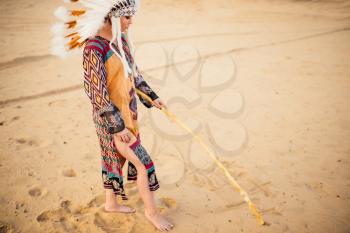 Young American Indian woman draws signs on the sand, Cherokee, Navajo. Headdress made of feathers of wild birds