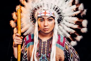 Portrait of young American Indian woman on sunset. Cherokee, Navajo, west native culture. Headdress made of feathers of wild birds.