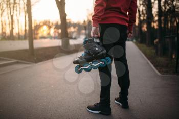 Male person hands with roller skates, city park on background. Male rollerskater with rollerskates