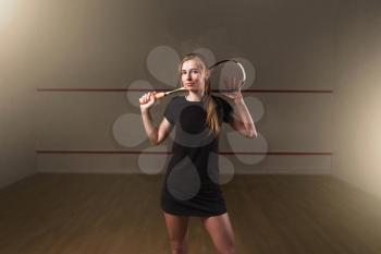 Attractive young woman with squash racket, indoor training club on background