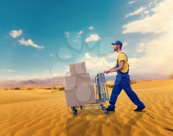 Male courier with trolley in desert. Distribution business. Cargo delivery. Empty, clear containers. Logistic service