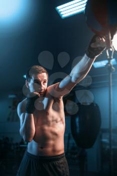 Boxer in bandages training with bag in gym. Boxing workout, mens sport