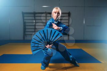 Female wushu master with fan, martial arts. Woman in blue cloth on fight training