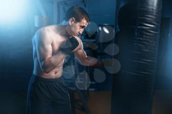 Man in black handwraps exercises with bag in gym. Boxing workout, mens sport