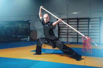 Wushu master training with spear, martial arts. Man in black  cloth poses with blade