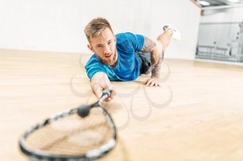 Squash training, male player with racket lies on the floor. Active sport workout. Game with ball and racquet