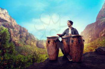 Young male drummer with wooden bongo drums plays in desert valley, musician in motion. Djembe, musical percussion instrument, ethnic music