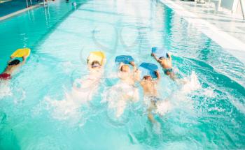 Boys swimming with plank in a pool race. Children in water with plank are doing swim exercise. Healthy sport activity in pool. Sportive kids activity in modern sport center with pool.
