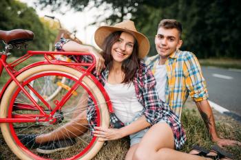 Love couple with vintage bikes sitting on roadside. Romantic journey of young man and woman. Boyfriend and girlfriend together outdoor, retro bicycle