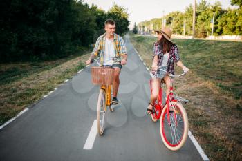 Smiling love couple riding on retro bikes in summer park, romantic date of young man and woman. Boyfriend and girlfriend together outdoor, vintage bicycle