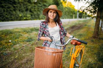Pretty woman in hat against yellow vintage bicycle with basket, green summer park. Cycling outdoor. Girl on retro cycle