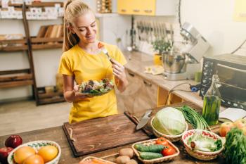 Happy woman cooking salad on the kitchen, healthy bio food preparing. Vegetarian diet, fresh vegetables and fruits on wooden table