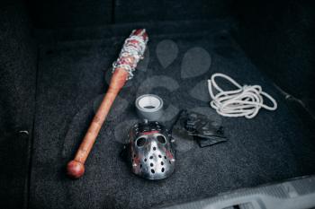 Psycho man instruments in opened car trunk, maniac. Hockey mask, baseball bat wrapped with bloody metal chain, leather fingerless gloves, duct tape and rope, serial murderer collection