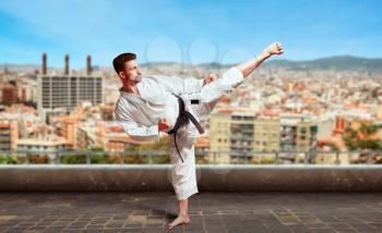 Martial arts, karate fighter in white kimono with black belt, karate training on the top of the roof
