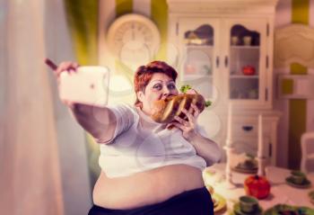 Fat woman eats sandwich and makes selfie, obesity, overweight people. Unhealthy lifestyle, fatty female