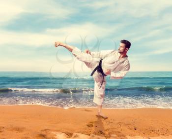 Martial arts, fighter in white kimono with black belt, training on the coast