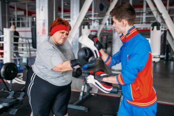 Overweight woman in gloves boxing with instructor in gym. Calories burning, obese female person on hard training in sport club