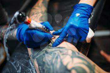 Female tattooist makes tattoo by machine on male shoulder. Professional tattooing in salon