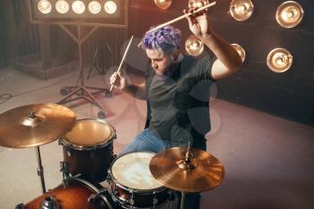 Bearded drummer with colorful hair on the stage with lights, vintage style. Musical performer, live music performing