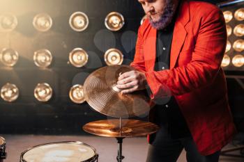 Bearded drummer in red suit on the stage with lights, retro style. Musical performer with colorful hair, drum instrument