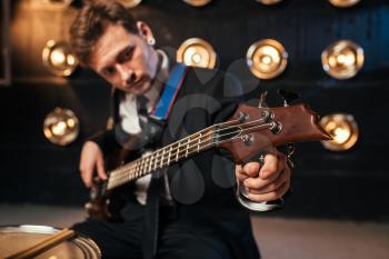 Rock guitarist in suit playing on bas-guitar, stage with lights on background, retro style. Live music performer